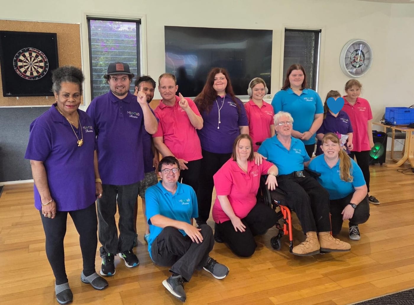 A community theatre group together in the hall in their matching shirts.