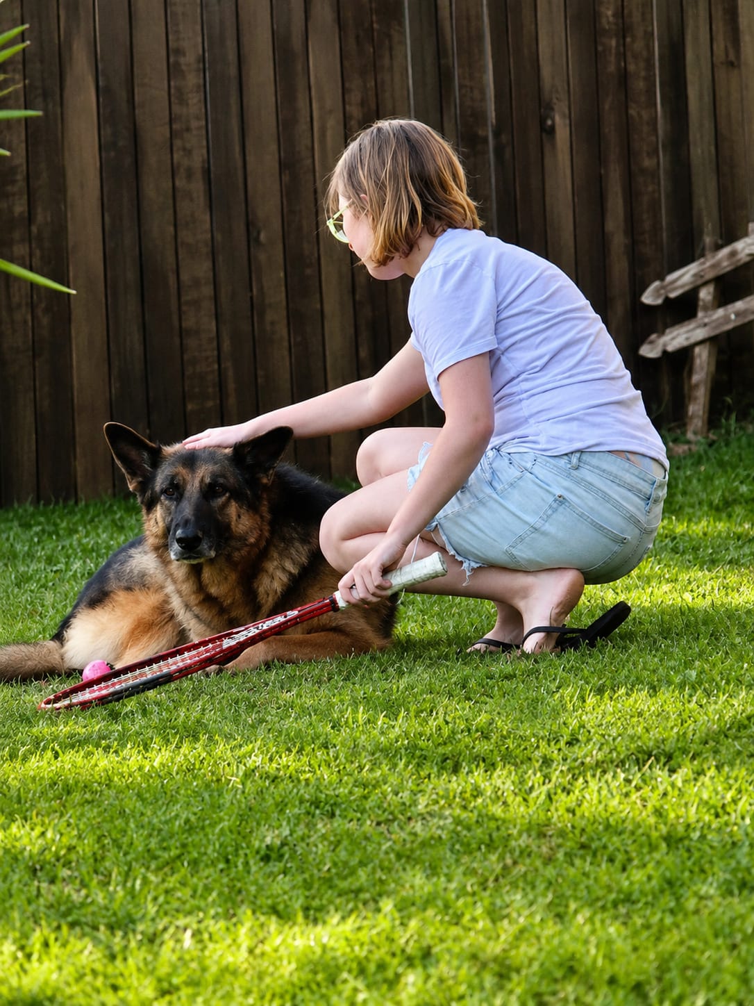Crouching on the lawn beside the family dog, a tennis racquet resting on the grass.
