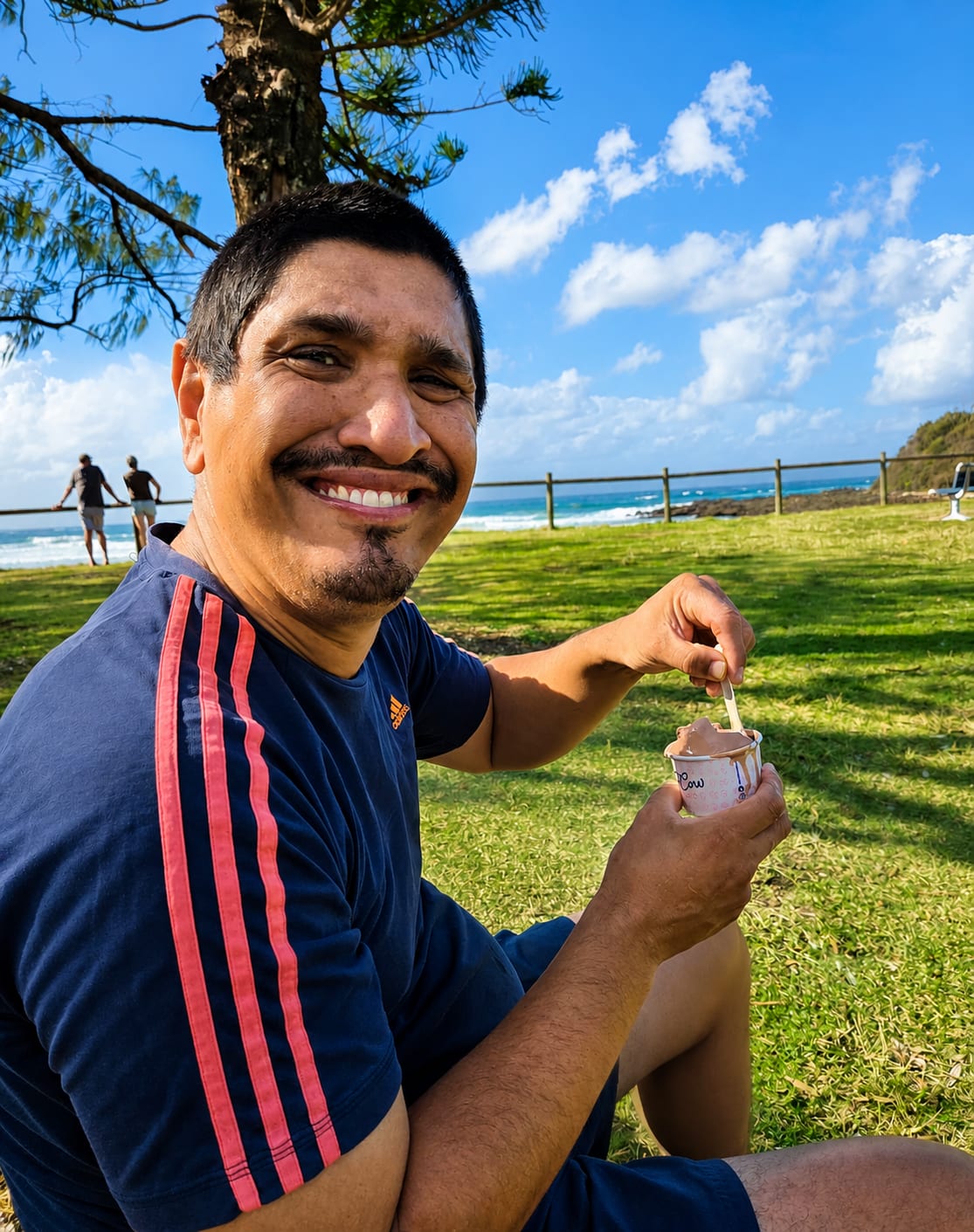 Sitting on the grass at a coastal park with an ice cream, the ocean behind.
